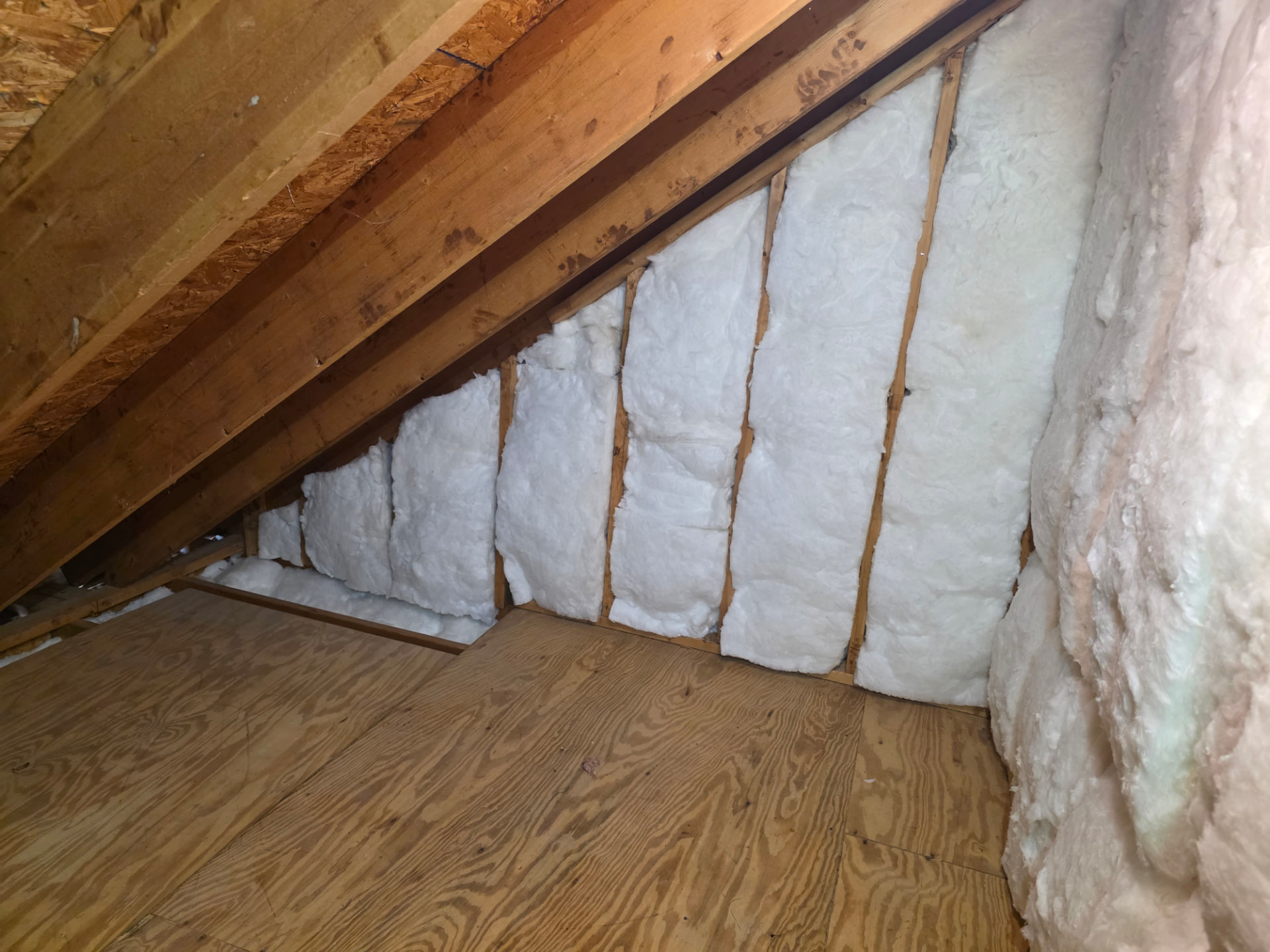 Finished attic batt insulation fitted between wall studs beneath sloped rafters